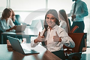 Businesswoman shows thumbs up in office. Alright gesture from young smiling girl. Group of businesspeople work on