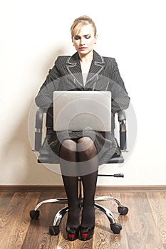 Businesswoman sits on chair with her laptop on wallpaper background