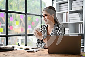 A businesswoman sits at her office desk and daydreams while sipping her morning coffee