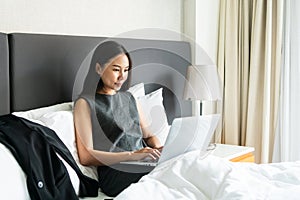 Businesswoman sitting on bed in hotel room while working on computer. Business trip, work from home concept