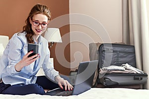 Businesswoman working in hotel room, using laptop and mobile phone