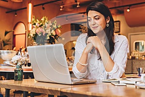 Businesswoman sitting in cafe at table,looking on screen of computer, smiling. Distance work. Online marketing,education