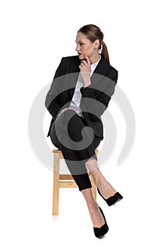 Businesswoman sitting with crossed legs and looking aside intrigued