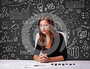 Businesswoman sitting at desk with business scheme and icons