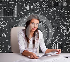 Businesswoman sitting at desk with business scheme and icons