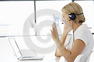 Businesswoman Sitting At Desk In Office Using Laptop Wearing Headset photo