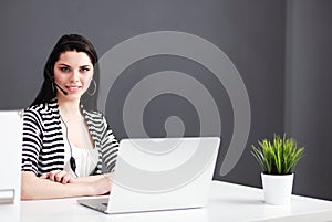 Businesswoman sitting at desk in office using laptop wearing headset photo