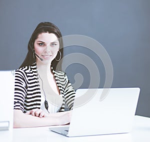Businesswoman sitting at desk in office using laptop wearing headset photo