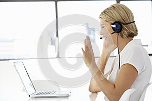 Businesswoman Sitting At Desk In Office Using Laptop Wearing Headset