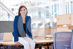 Businesswoman sitting on the edge of desk smiling warmly