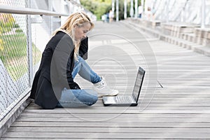 Businesswoman sitting on the floor of the street using a laptop