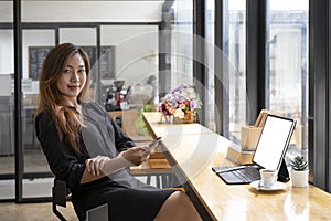 Businesswoman sitting in front of laptop computer at cafe and using mobile phone.