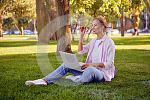 Businesswoman sitting grass summer park using laptop Business person working remote. Outdoor