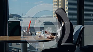 Businesswoman sitting in the office at lunch by the panoramic window, uses a mobile phone. Business woman at lunch time