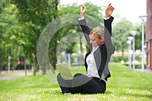 Businesswoman sitting outdoors with laptop and arms up in celebration