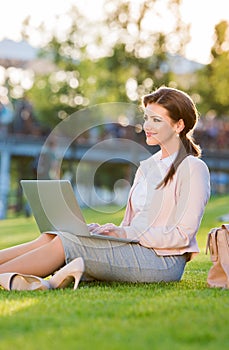 Businesswoman sitting in park working on laptop, sunny summer da