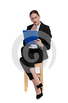 Businesswoman sitting and reading something on clipboard intrigued