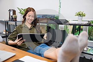 Businesswoman sitting relaxing reclining with feet up on computer desk reading report