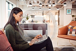 Businesswoman Sitting On Sofa Working On Laptop At Desk In Shared Workspace Office