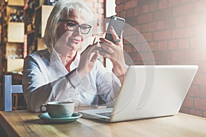 Businesswoman is sitting at table in front of laptop and using smartphone. Education for adults. Pensioner freelancer