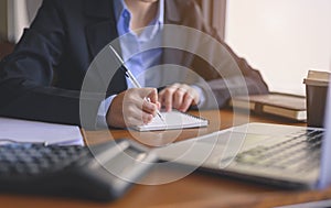 Businesswoman sitting to working at office desk with calculator and laptop writing something while working.