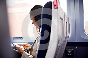 Businesswoman Sitting In Train Commuting To Work Checking Messages On Mobile Phone