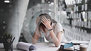 Businesswoman sitting in workplace and holding head with hands feeling desperate or suffers from headache.