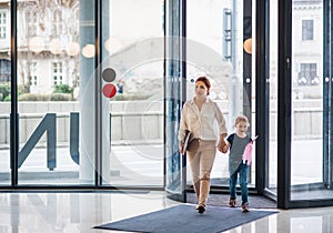 A businesswoman with small daughter entering office building, walking.