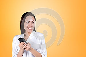 Businesswoman with smartphone in hands, happy on empty yellow background