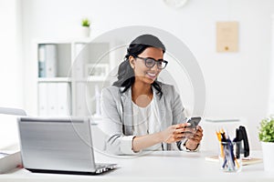 Businesswoman with smartphone and laptop at office