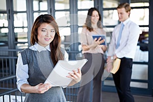 Businesswoman smiling at camera while her colleagues discussing in background