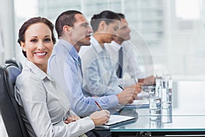 Businesswoman smiling at camera while her colleagues listening t