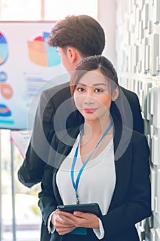 Businesswoman standing in front looking at camera with man in the background for female leadership concept