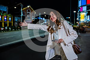 businesswoman standing hail waving hand taxi on road in busy city street at night