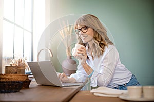 Businesswoman standing in the kitchen and using laptop while working from home