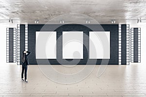 Businesswoman standing in modern gallery interior with three empty billboards