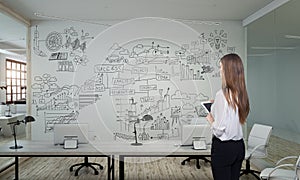 A businesswoman standing in modern office with creative business strategy sketch drawn on white wall