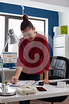 Businesswoman standing near desk in startup office looking at charts.