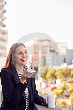 Businesswoman Standing Outside Office Building Using Mobile Phone With City Skyline In Background