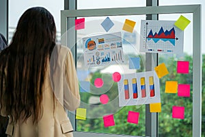 Businesswoman standing and presenting idea with sticky note on glass wall in meeting in the office. multinational business people