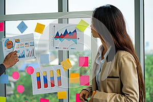 Businesswoman standing and presenting idea with sticky note on glass wall in meeting in the office. multinational business people