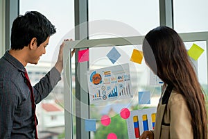 Businesswoman standing and presenting idea with sticky note on glass wall in meeting in the office. multinational business people