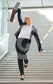 Businesswoman standing on staircase with arm raised in celebration