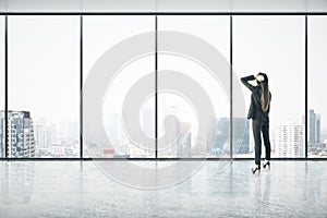 Businesswoman standing thinking in an empty big office room with big windows and city view. Real estate and future success concept