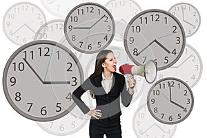 Businesswoman stands among clocks.