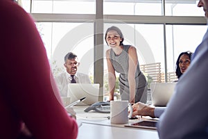 Businesswoman stands listening to colleagues at a meeting