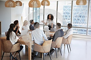 Businesswoman Stands To Address Meeting Around Board Table