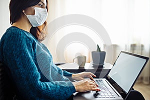 Businesswoman stays home and works during coronavirus epidemia quarantine. Female worker wearing a medical mask and typing on a