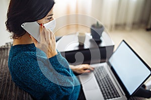 Businesswoman stays home and works during coronavirus epidemia quarantine. Female worker wearing a medical mask and typing on a