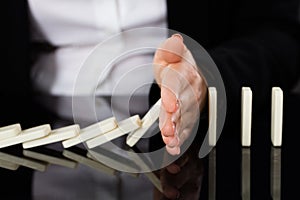 Businesswoman Stopping Dominoes On Desk